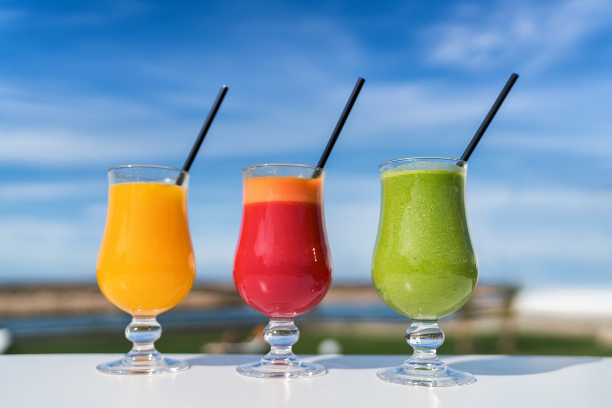 Healthy eating juicing cleanse diet trend concept - fruit and vegetable juice glasses on outdoor cafe table. Green smoothie or cold-pressed juices. Orange, beet and spinach green smoothie cups.